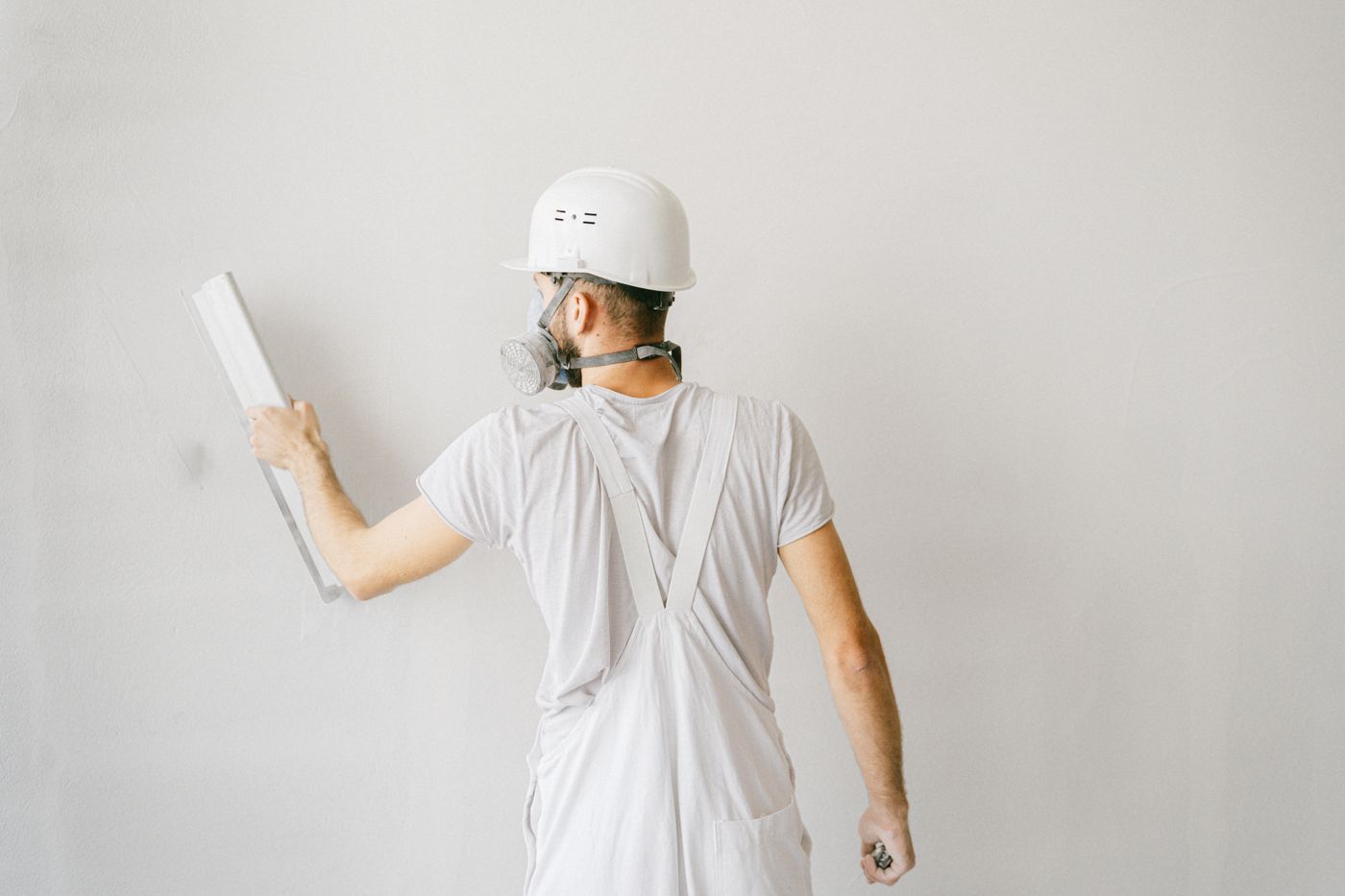 Stukadoor in witte overall werkt een witte wand af met een pleisterspaan